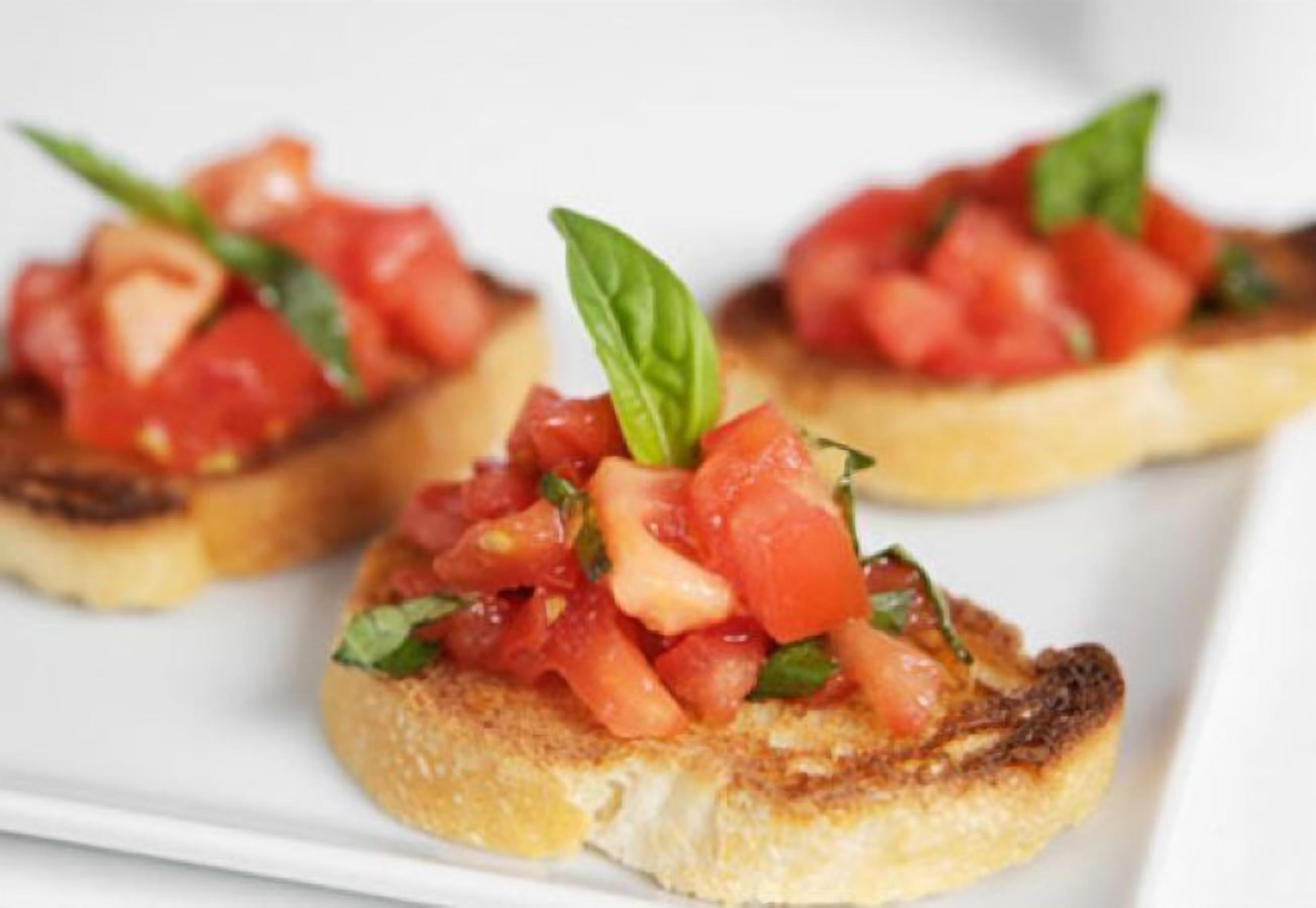 A plate with three pieces of toast topped with tomato and basil.