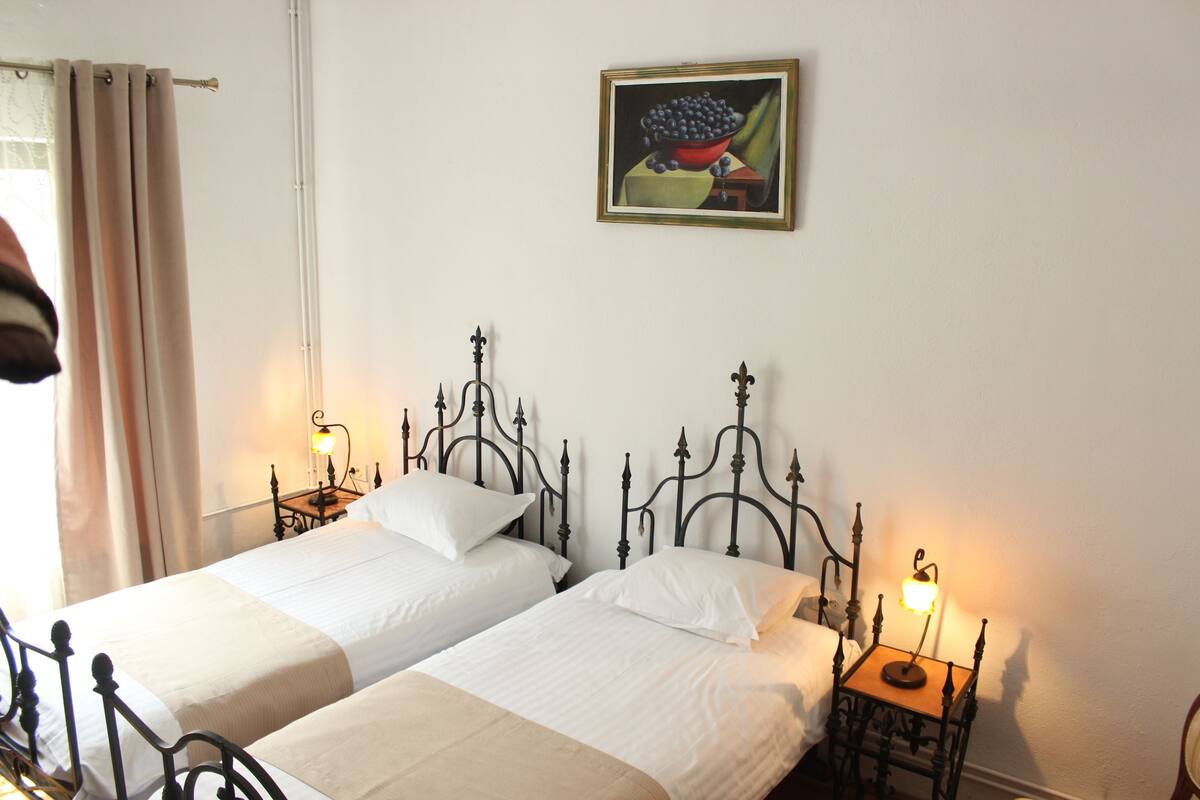 A room with two beds, each with a headboard and bedside tables. There is a painting on the wall above the beds.