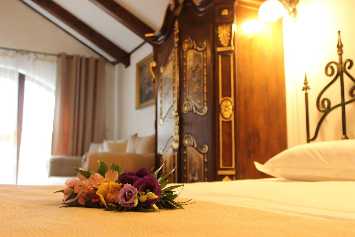 A hotel room with a bed, a wooden headboard, and a floral arrangement on the bed.