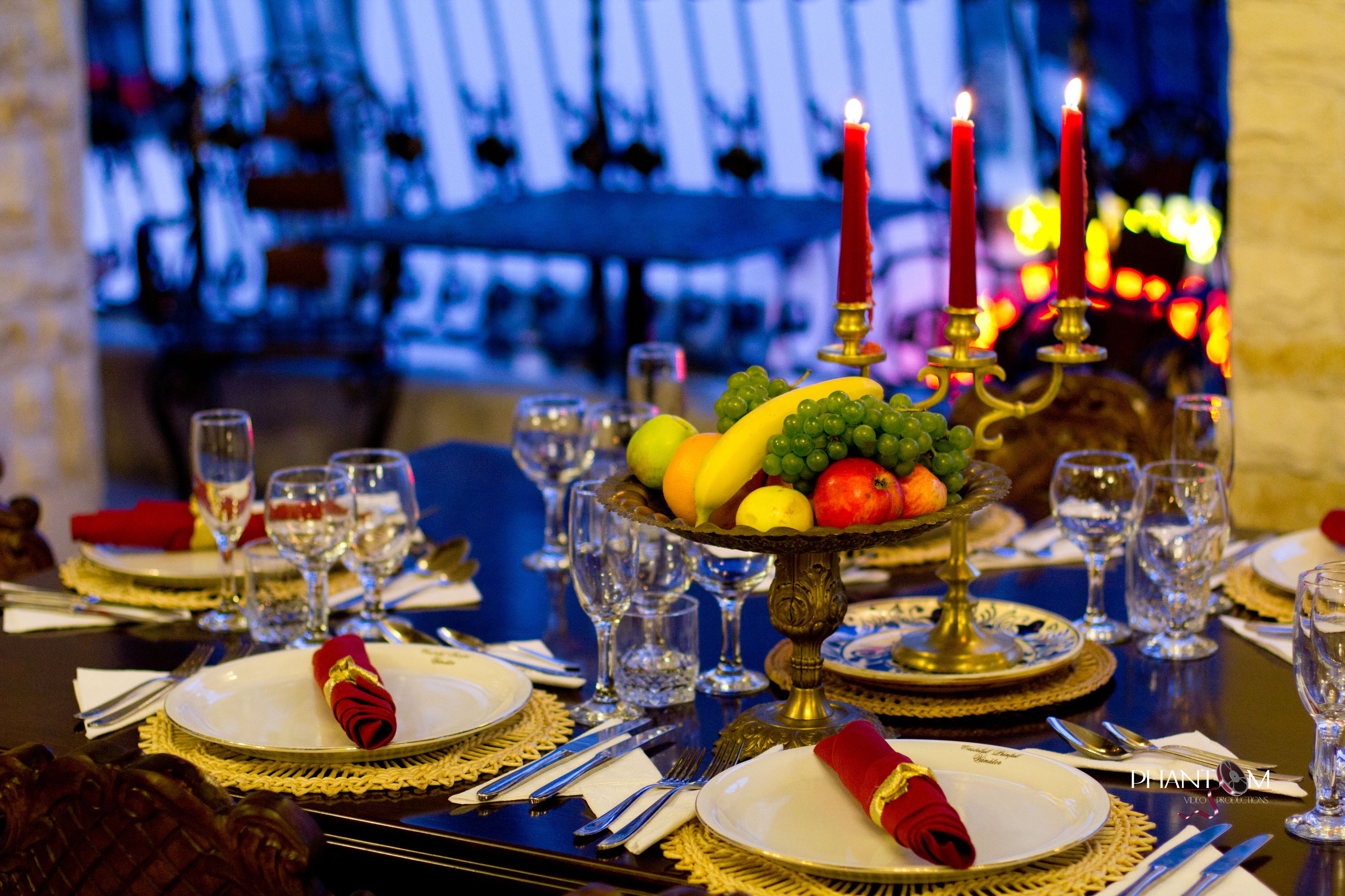 Une table à manger dressée avec des assiettes, des couverts, des verres et un centre de table composé de fruits.