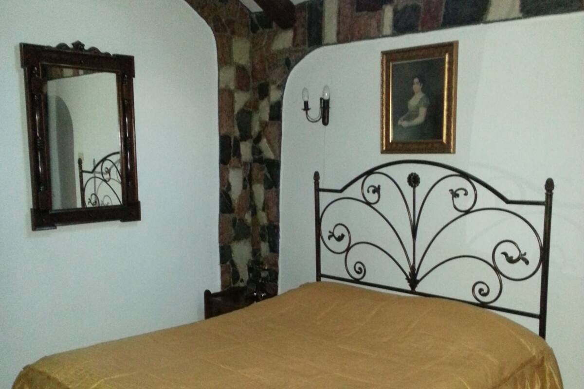 A bedroom with a bed, a mirror, a picture frame, and a stone wall.