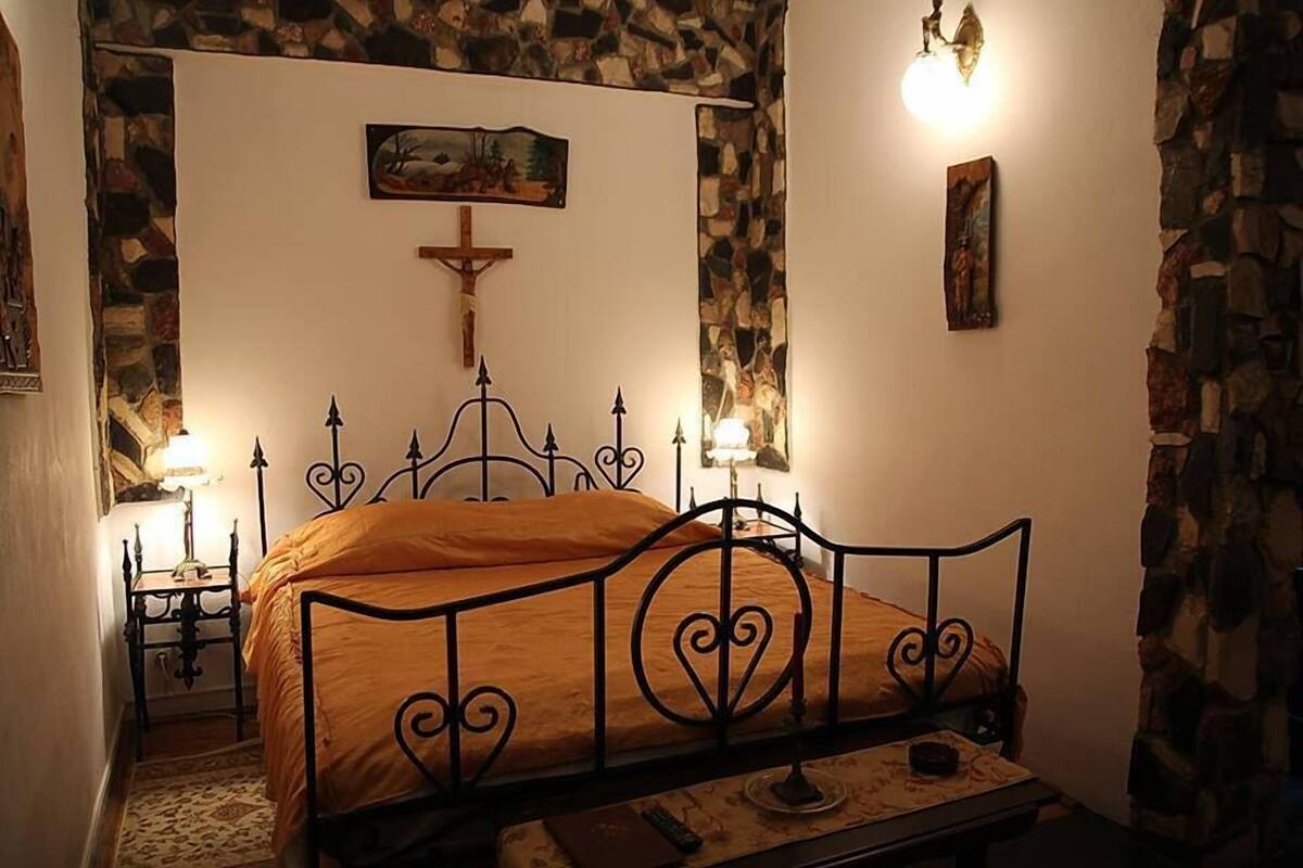 A bedroom with a metal bed frame, a wooden headboard, a stone wall, and a painting on the wall.