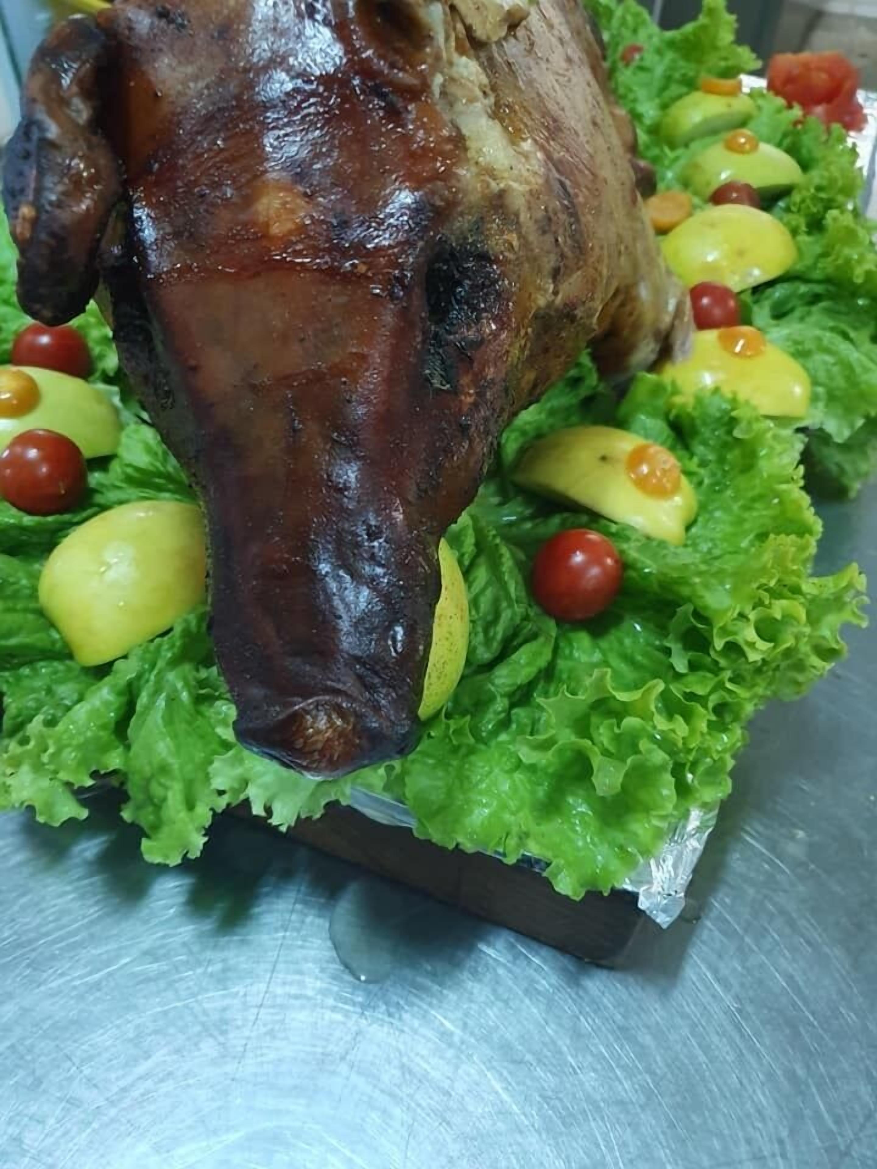 Un cerdo asado sobre una cama de lechuga con tomates cherry y rodajas de limón.