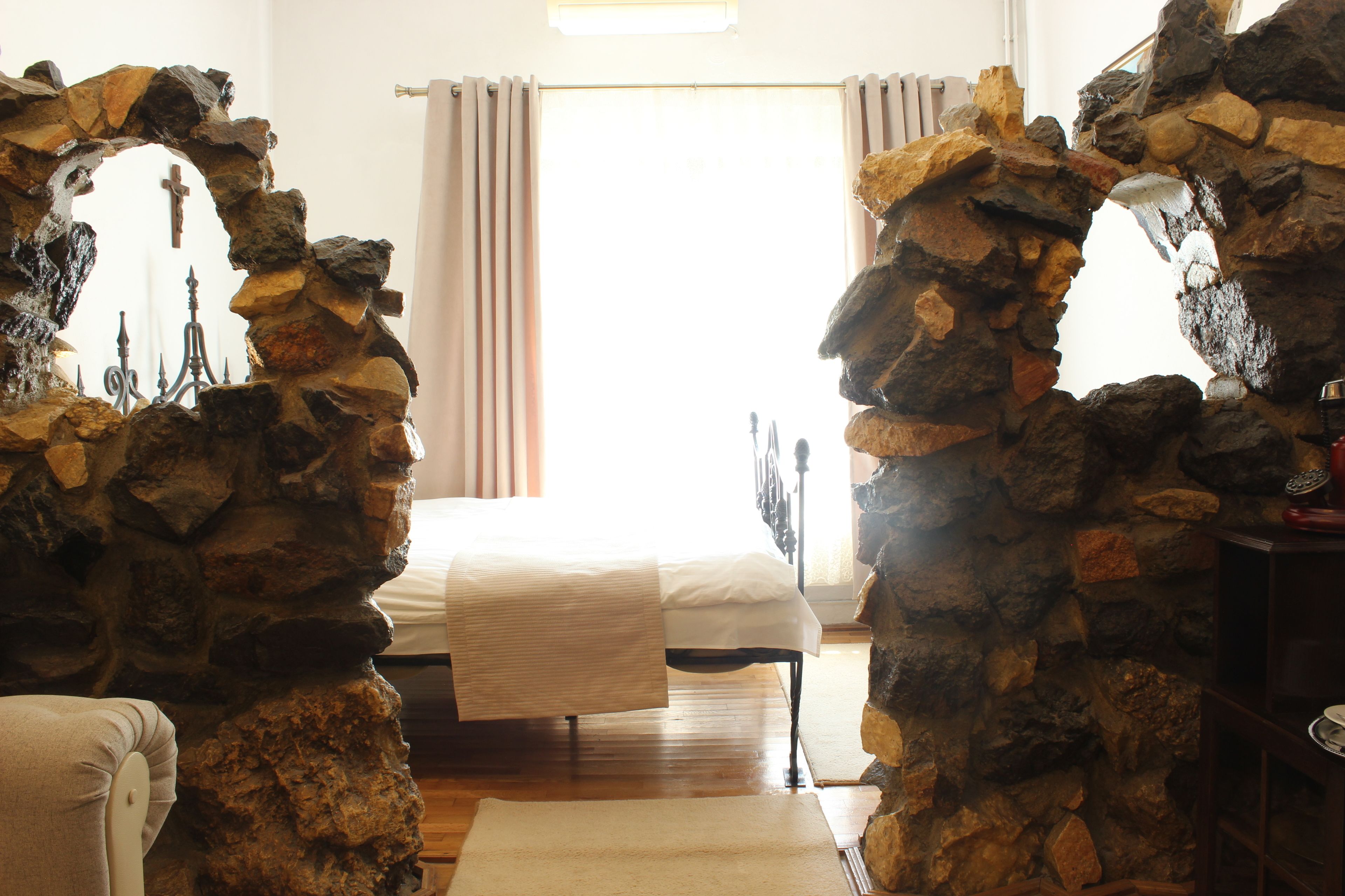 A bedroom with a stone archway, a bed, a nightstand, and a window with curtains.