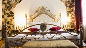 A bed with an ornate metal frame, a stone wall behind it, and a red curtain to the right. - Hunter Prince Castle Hotel  (Turda)