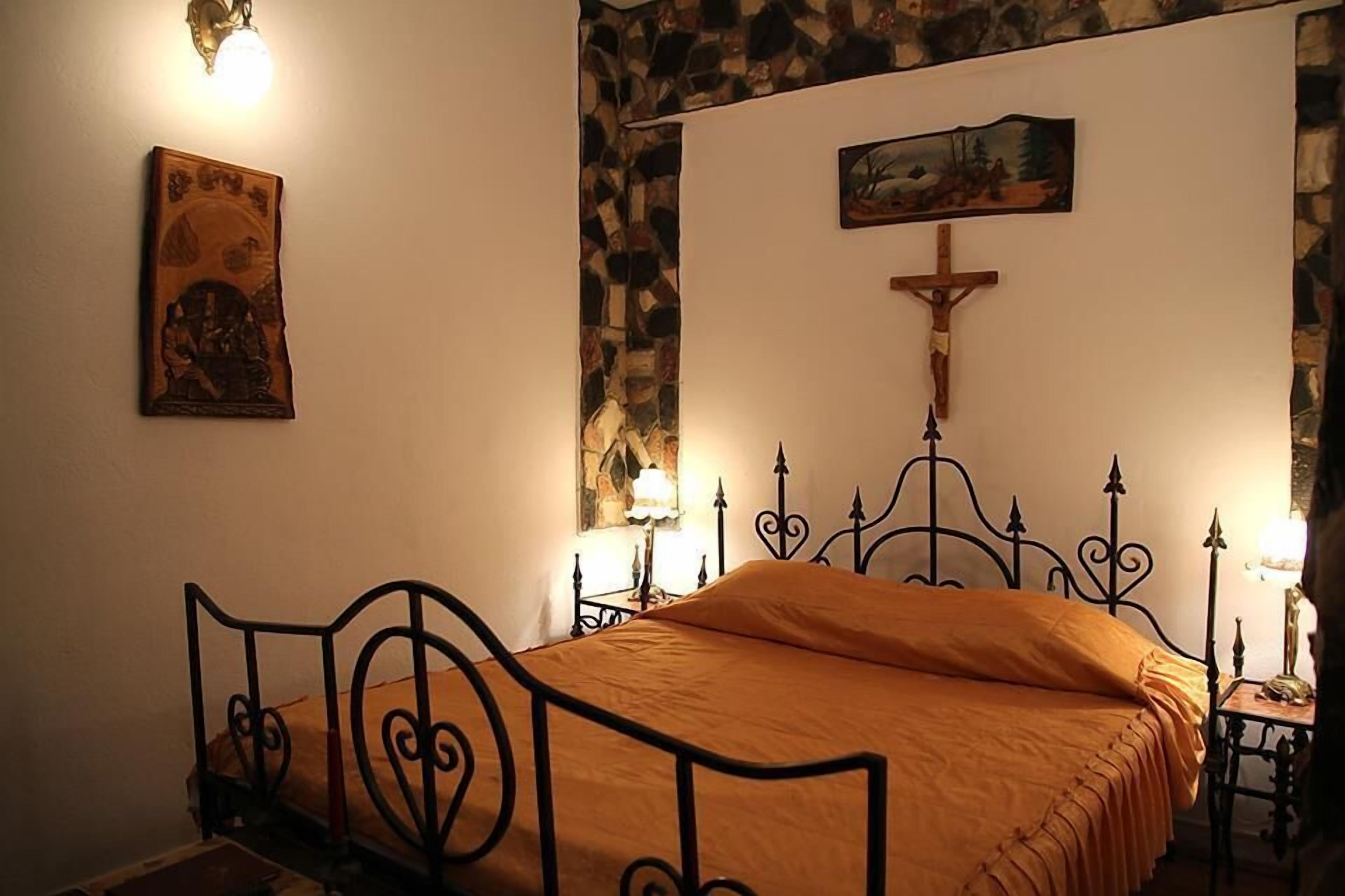 Un dormitorio con cama, una cruz en la pared y un cuadro sobre la cama.