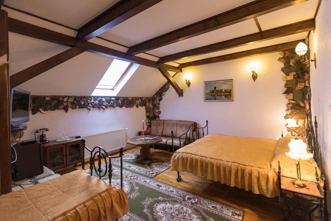 A cozy attic bedroom with a sloped ceiling, a stone wall, a wooden bed, a small sofa, a table, and a television.