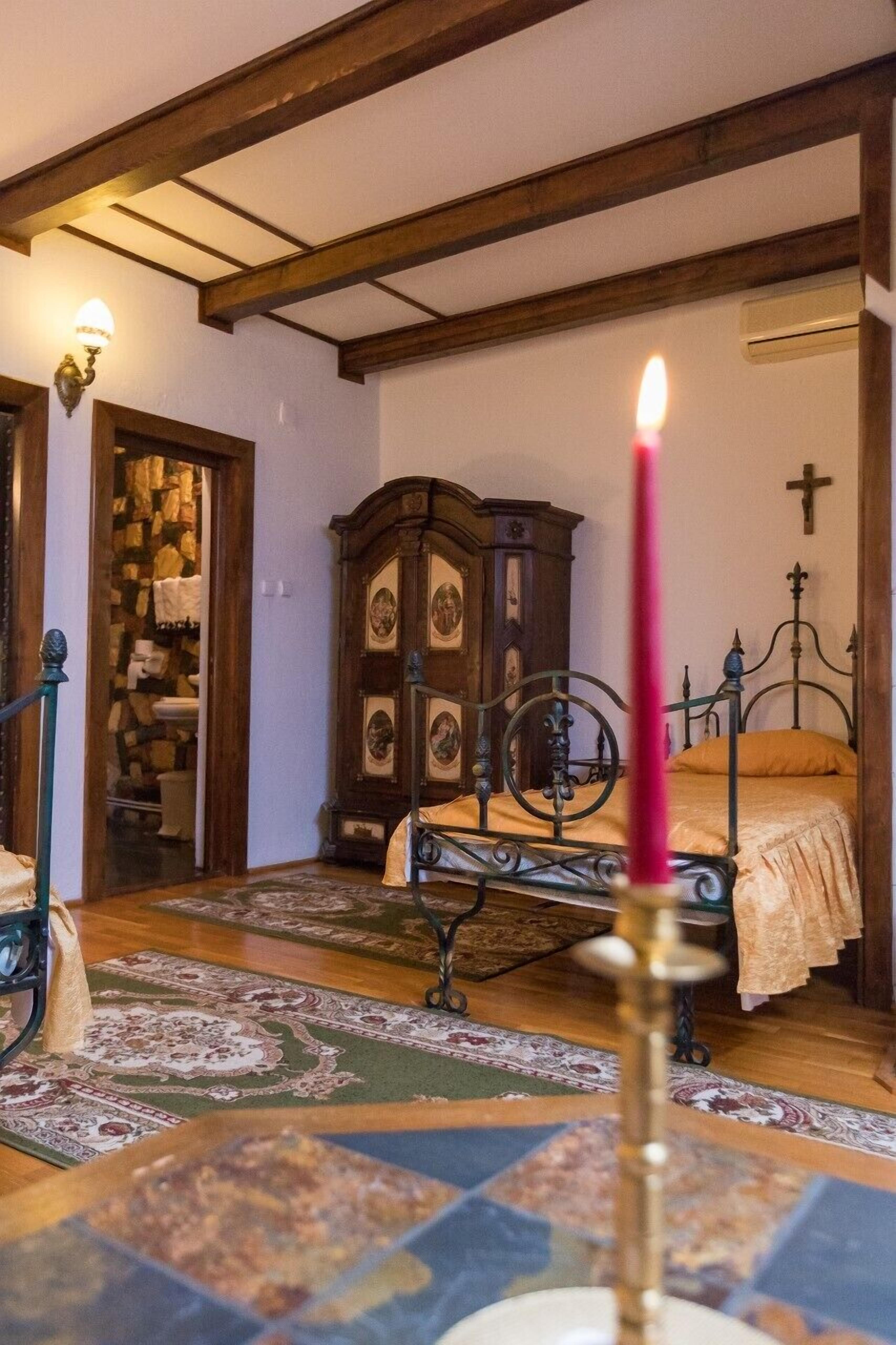 Een klassieke slaapkamer met een houten plafond, een metalen bed, een houten kast en een brandende kaars.