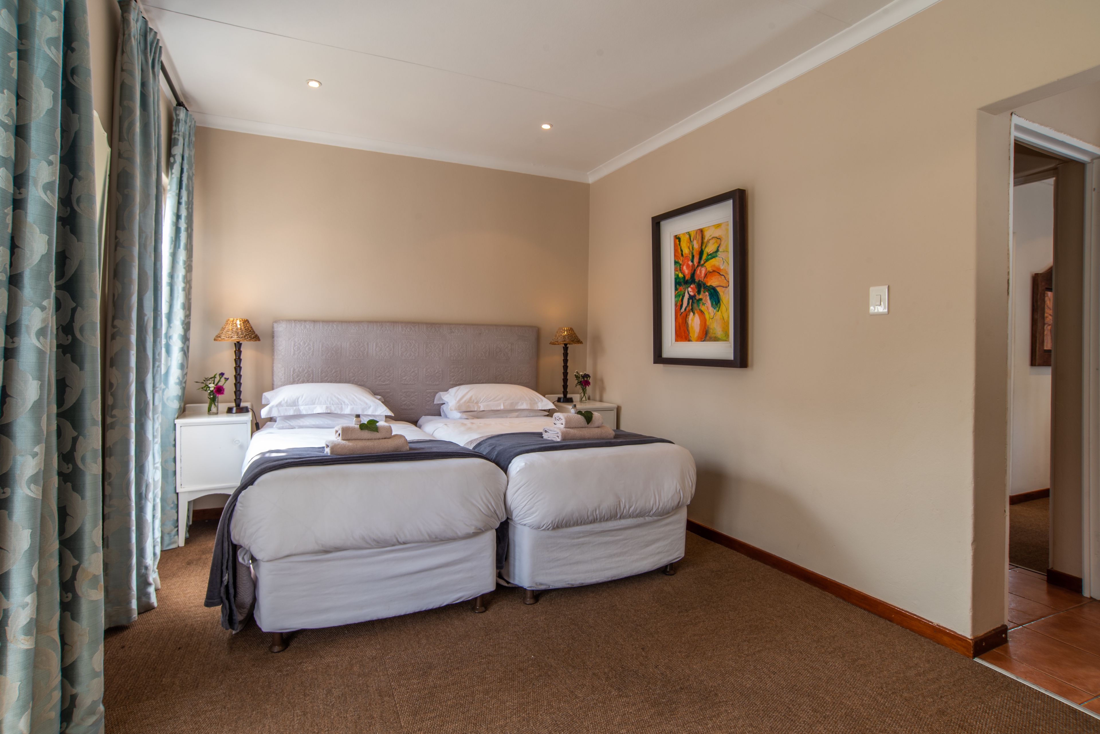 A hotel room with two beds, a nightstand with a lamp, a painting on the wall, and a carpeted floor.