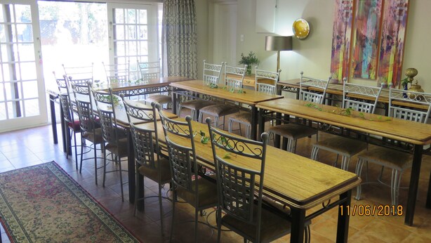 A dining area with multiple tables and chairs, a patterned rug, and a large window with curtains. - 5th Avenue Gooseberry Guest House (Randburg)