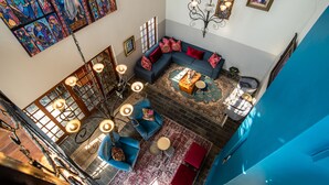 Ein großzügiger Wohnbereich mit einem blauen Sofa, roten Kissen, einem gemusterten Teppich und einer Chandelier.