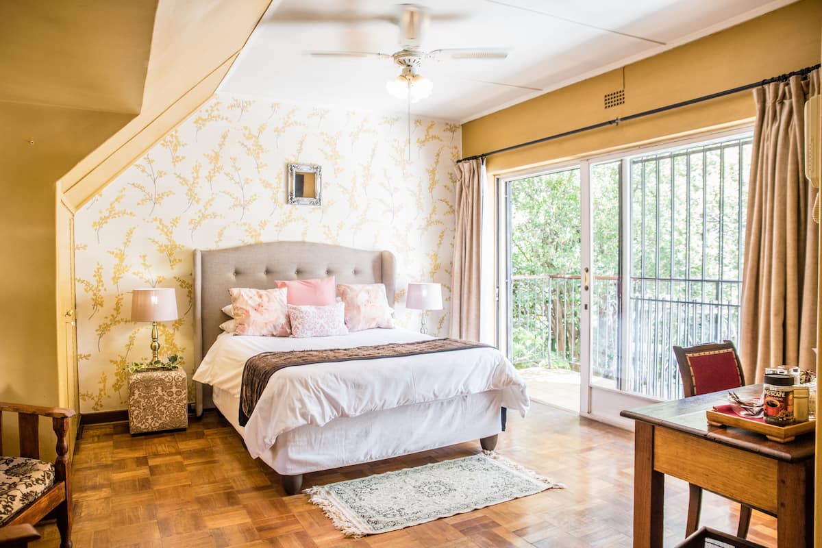 Une chambre avec un grand lit, un ventilateur de plafond, une fenêtre avec des rideaux et un plancher en bois.