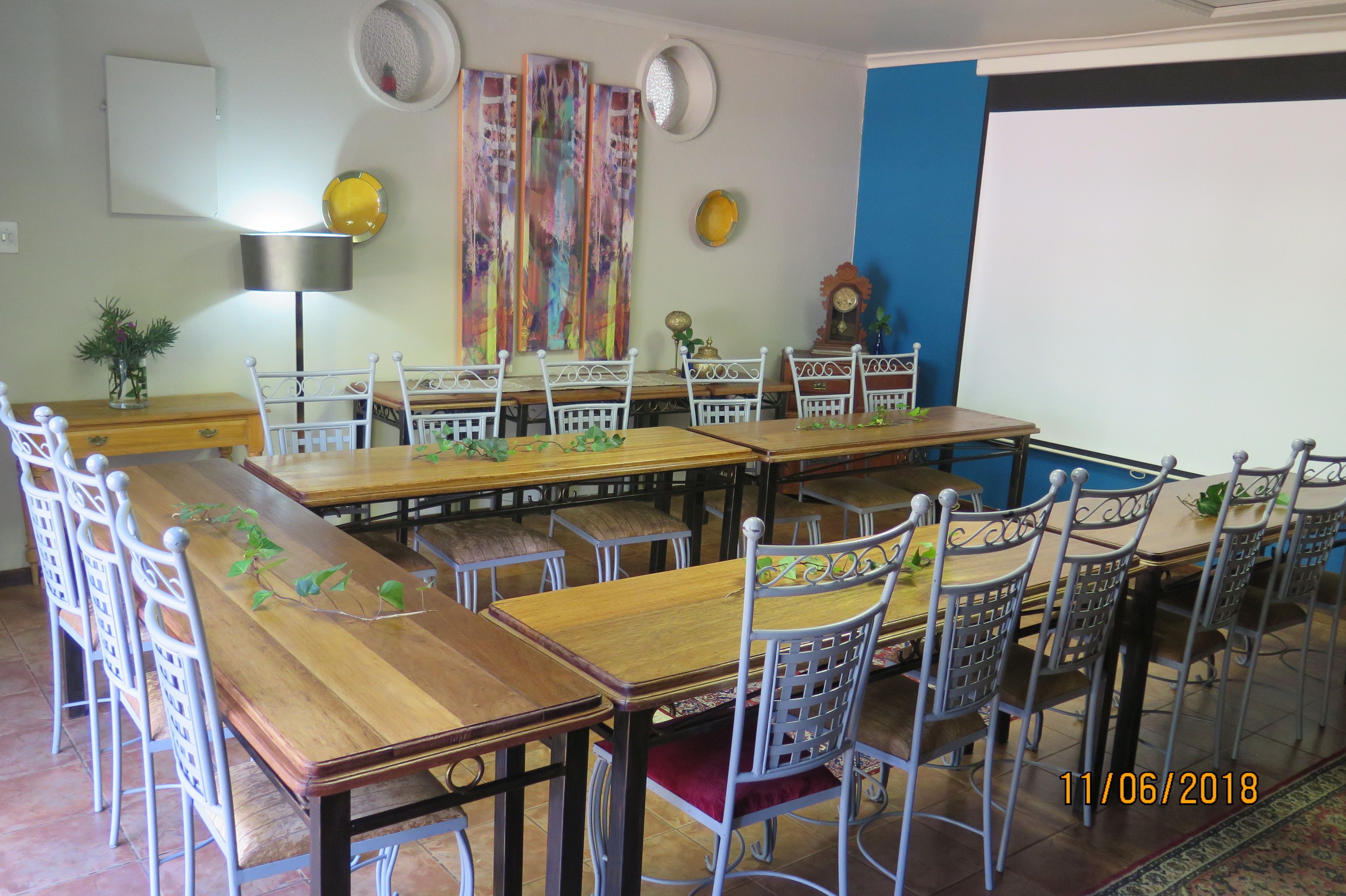 Un comedor con varias mesas de madera y sillas de metal blanco, una pantalla de proyector y decoración en la pared.