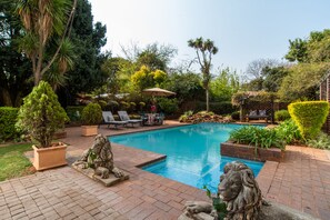 A swimming pool with a lion statue, surrounded by potted plants and a patio area with lounge chairs. - 5th Avenue Gooseberry Guest House (Randburg)