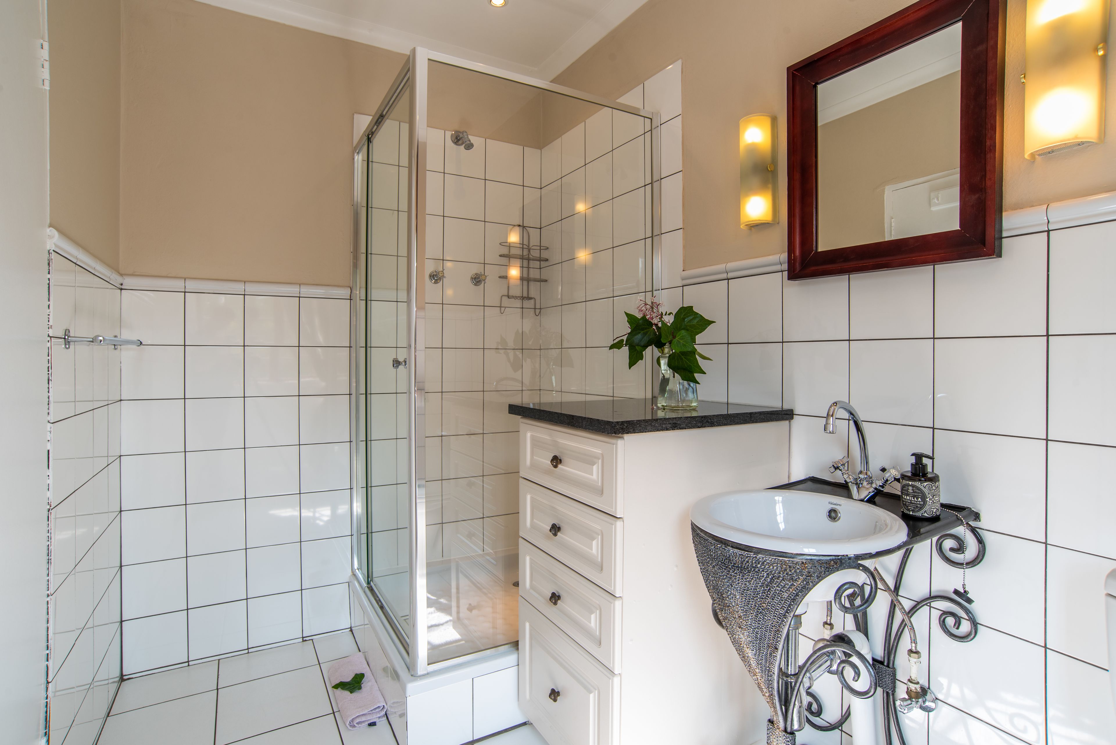 A bathroom with a glass shower enclosure, a sink with a decorative metal frame, and a mirror with wall-mounted lights.