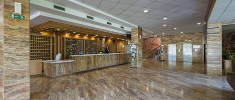 A hotel reception area with a marble floor, a reception desk, and a staircase leading to elevators.