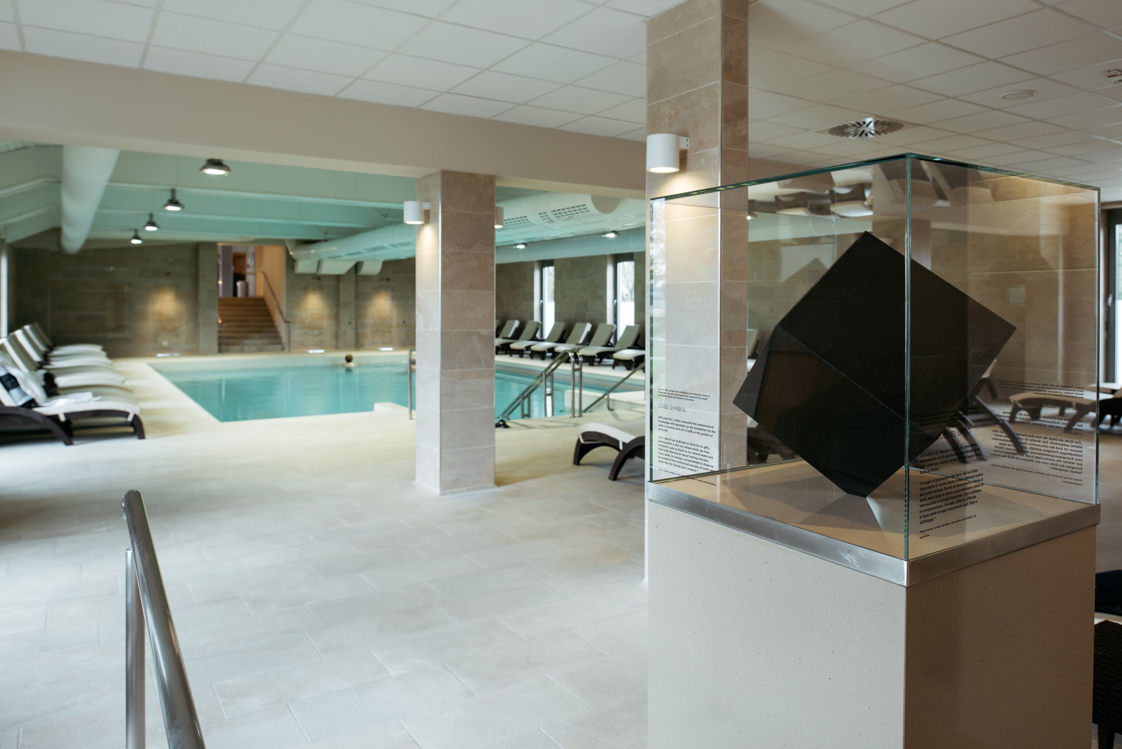 Zona de piscina interior moderna amb una vitrina de vidre i seients al costat de la piscina.