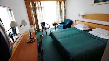 A hotel room with a bed, a desk with a chair, a small table with a chair, and a window with curtains.