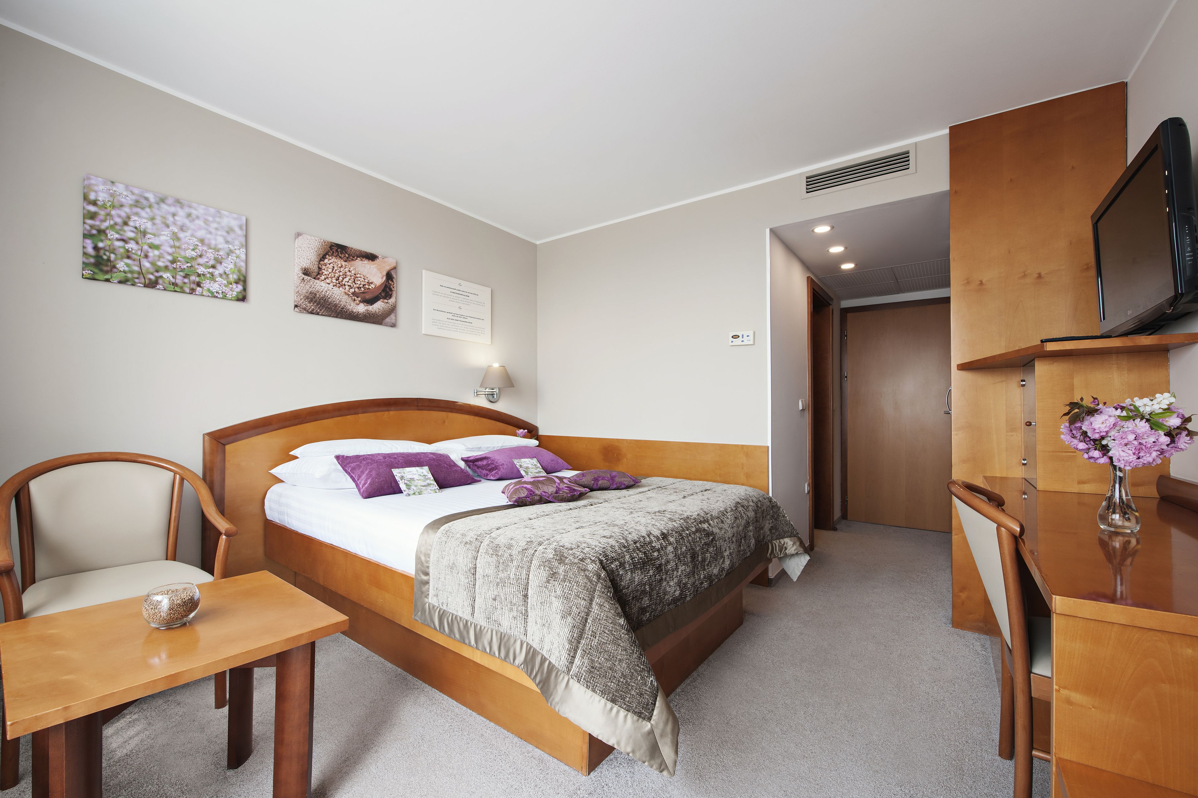A bedroom with a bed, bedside table, chair, and a TV on a wooden stand.