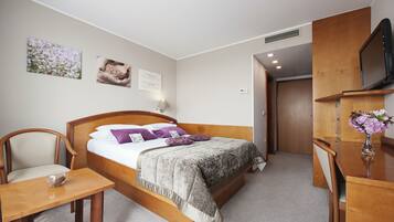 A bedroom with a bed, bedside table, chair, and a TV on a wooden stand.