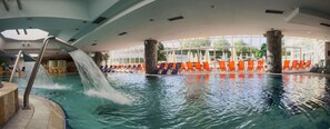 An indoor swimming pool with multiple lanes, a waterfall feature, and orange lounge chairs around the perimeter. - Hotel Livada Prestige - Sava Hotels & Resorts (Moravske Toplice)