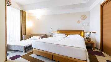 Une chambre d’hôtel avec un grand lit, un canapé-lit, une table de chevet avec une lampe et une petite plante en pot.