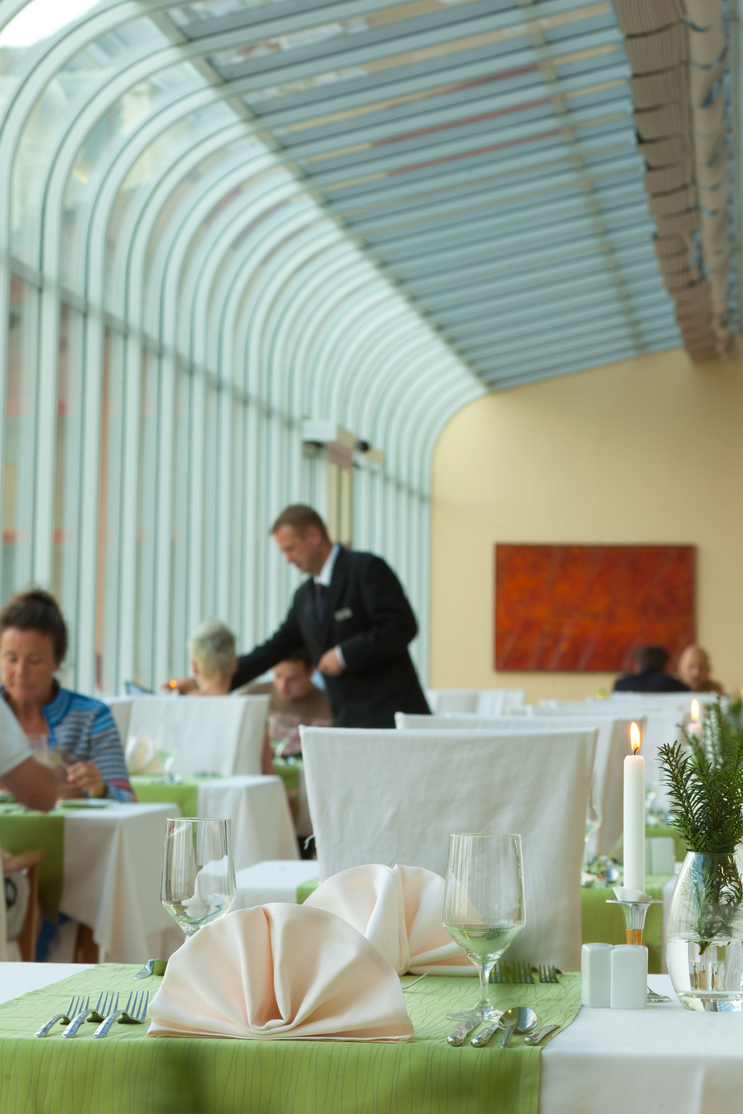 Un restaurant avec des tables dressées, un serveur en arrière-plan et une structure de plafond en verre.