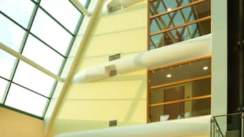 Un vestíbulo espacioso con techo alto, ventanas amplias, mostrador de recepción, zona de estar y exhibición de material informativo.