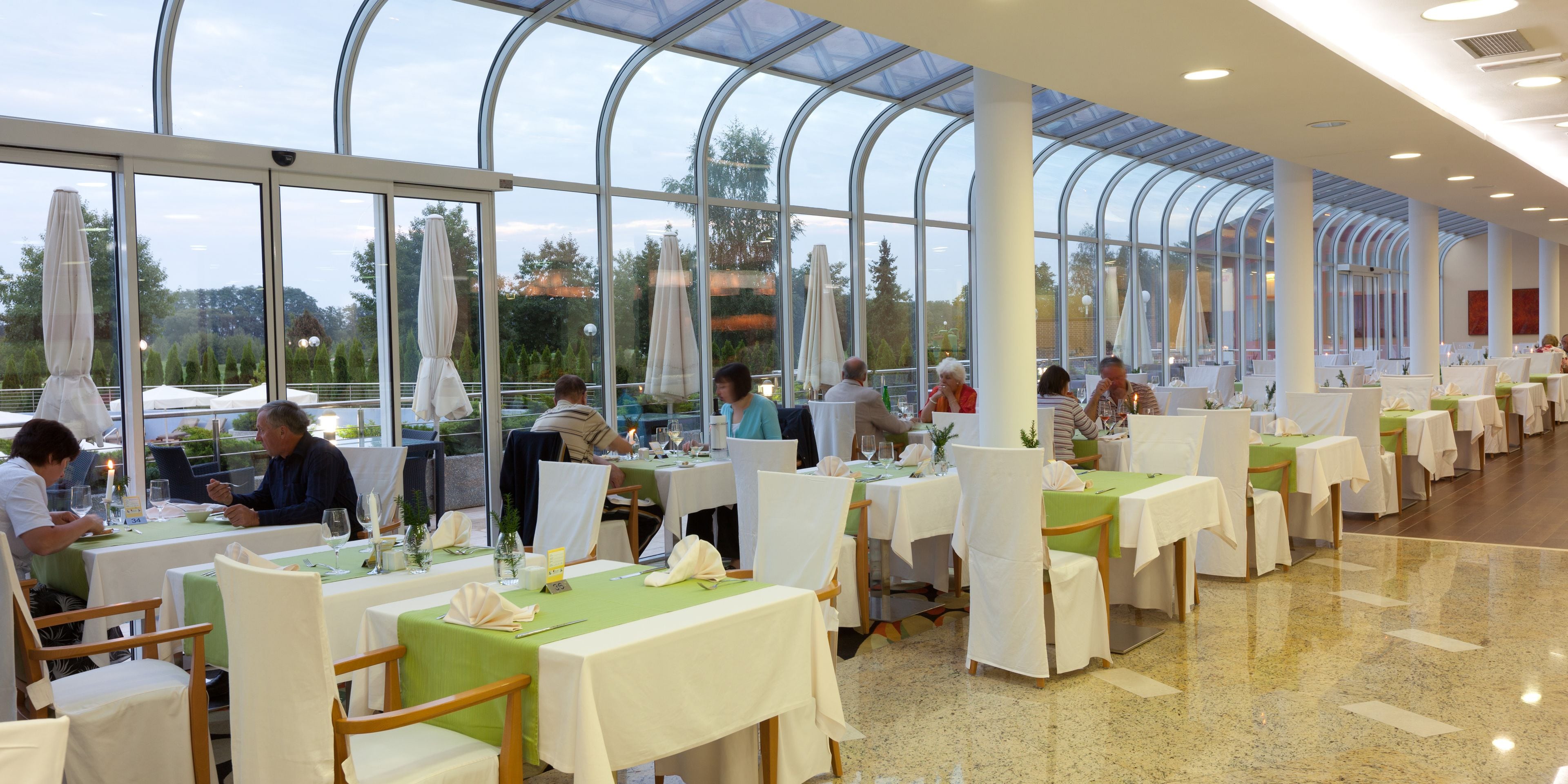 Un restaurante con techo de vidrio, mesas con manteles blancos y sillas cubiertas de blanco.