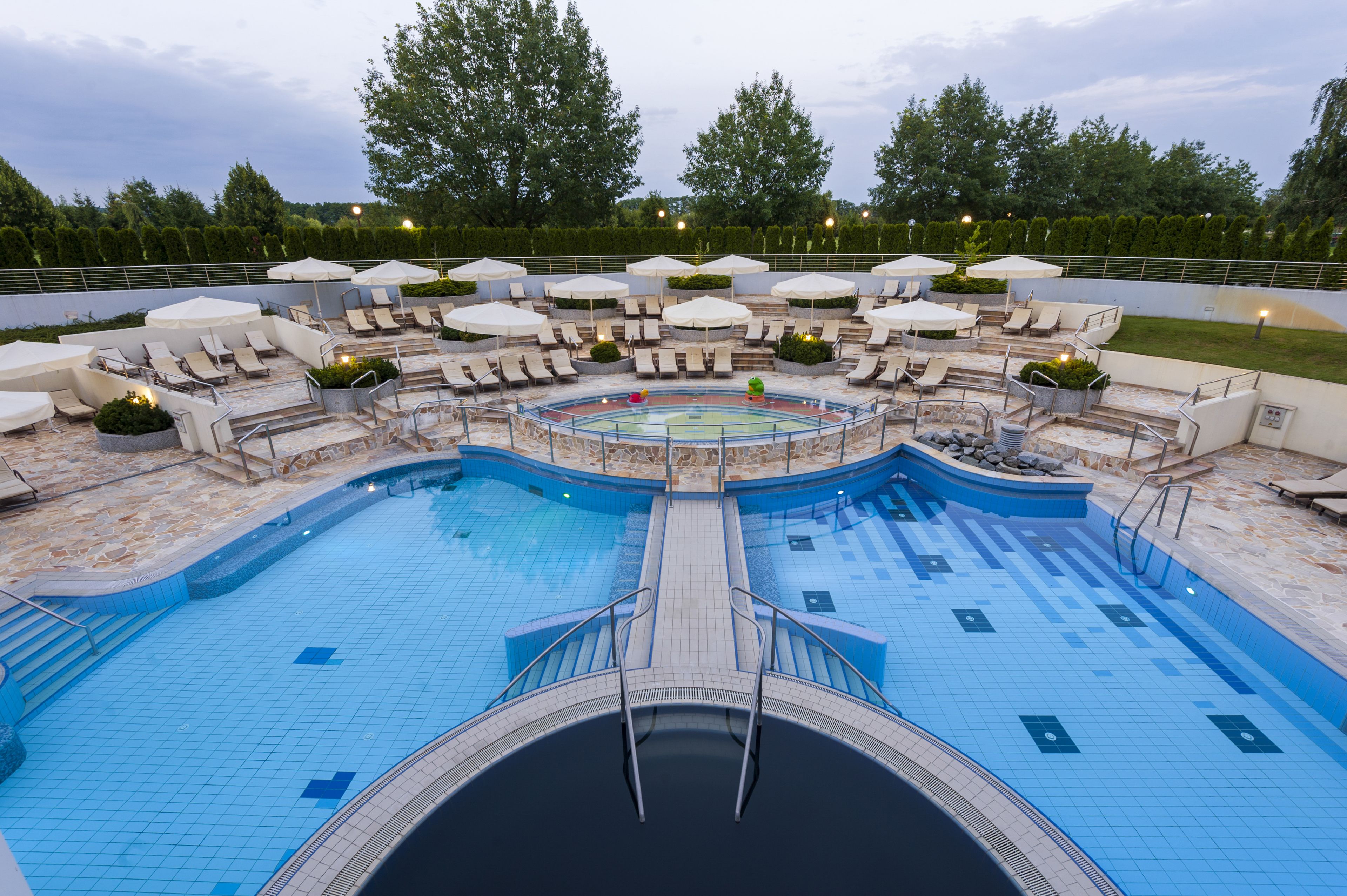 A swimming pool with lounge chairs and umbrellas, surrounded by a landscaped area with trees.