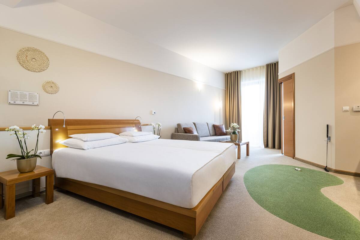 Une chambre d’hôtel avec un grand lit, un canapé, une petite table et une moquette verte.