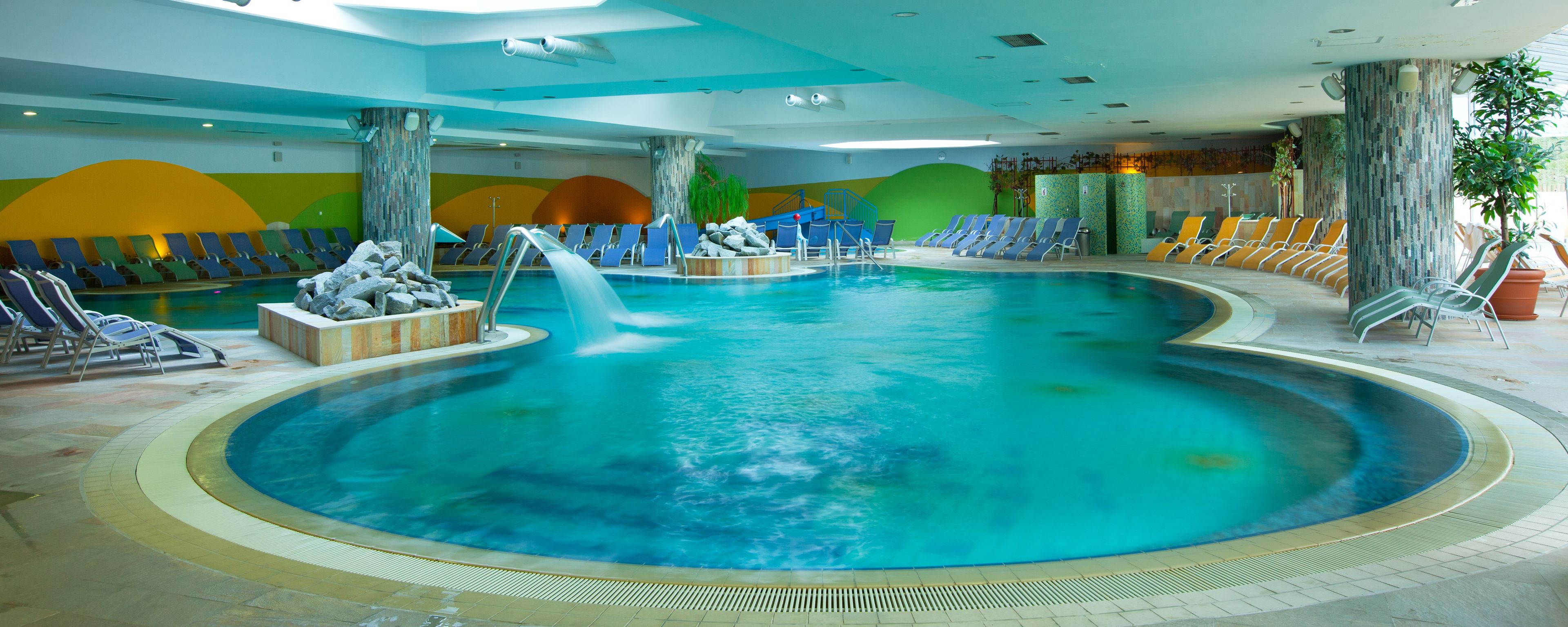 An indoor swimming pool with multiple lanes, lounge chairs, and a water slide.