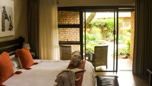 A hotel room with a bed, a desk, and a view of a garden through a sliding door. - Dreamfields Guesthouse (Mbombela)