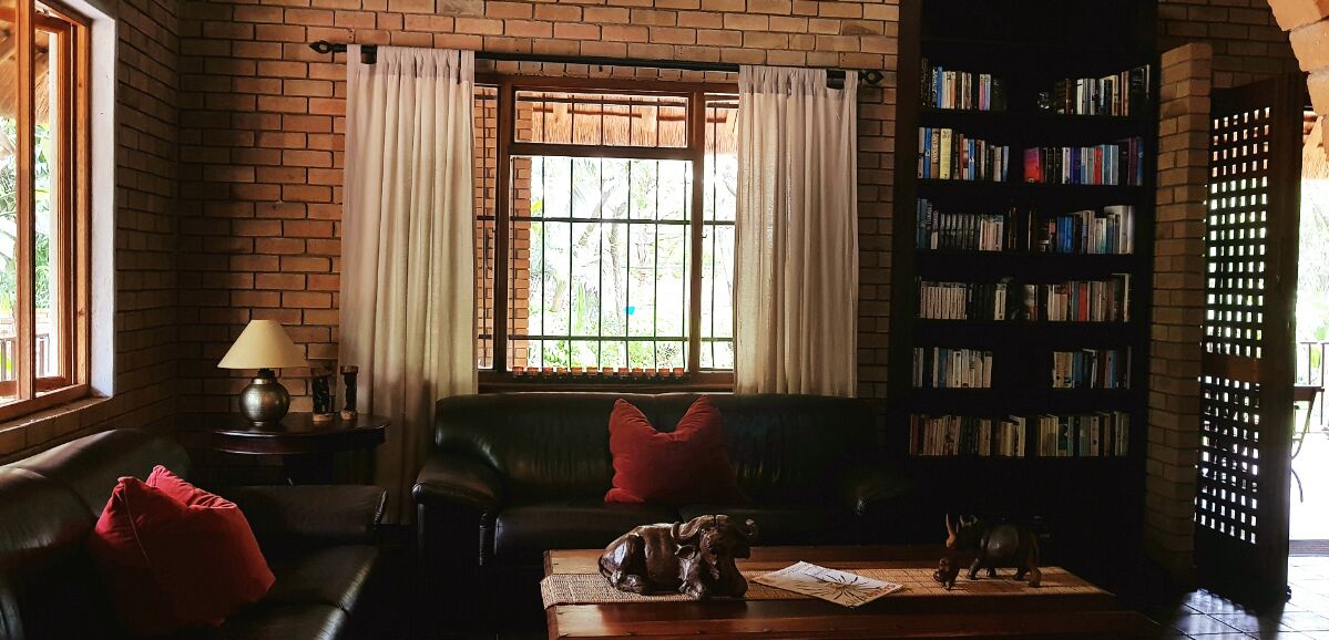 A cozy living room with a leather sofa, a coffee table with decorative items, a bookshelf, and a window with curtains.