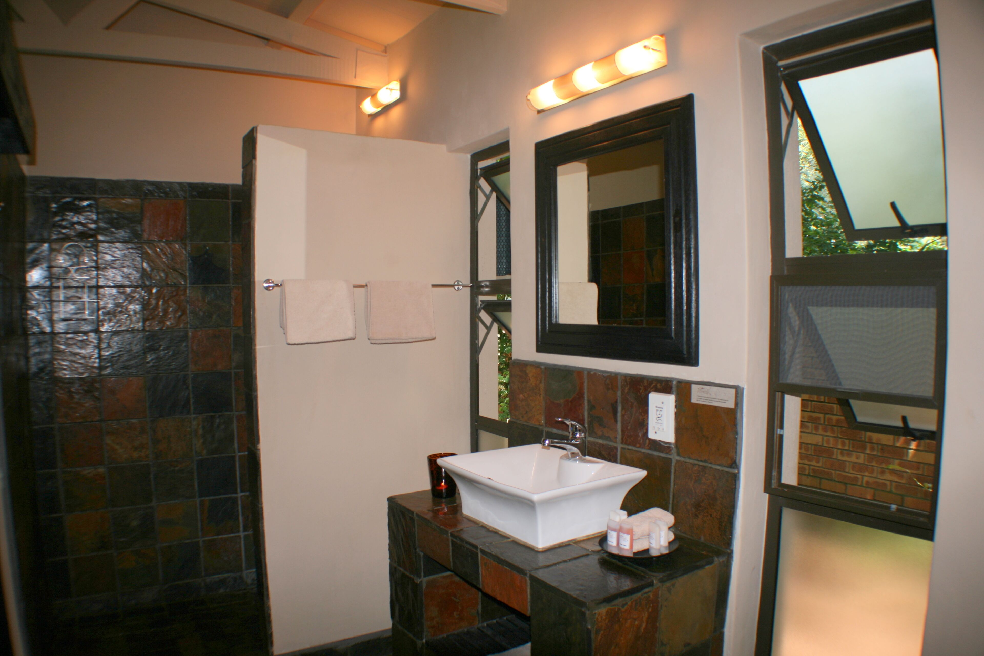 A bathroom with a white sink, a mirror, and a shower with a tiled wall.