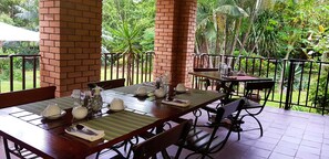 A dining area with brick pillars, tables set with white dishes, and a view of lush greenery. - Dreamfields Guesthouse (Mbombela)
