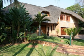A house with a thatched roof, brick walls, and a small front porch. - Dreamfields Guesthouse (Mbombela)