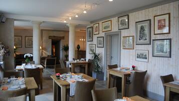 A dining area with multiple tables and chairs, framed pictures on the walls, and a column in the center.