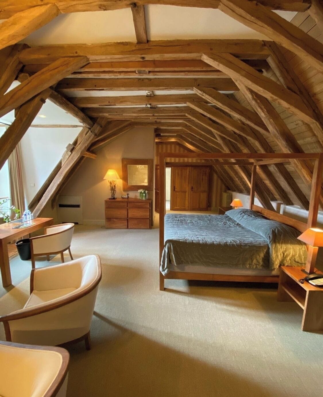 An attic bedroom with a wooden ceiling, a bed with a canopy, a desk, and a chair.