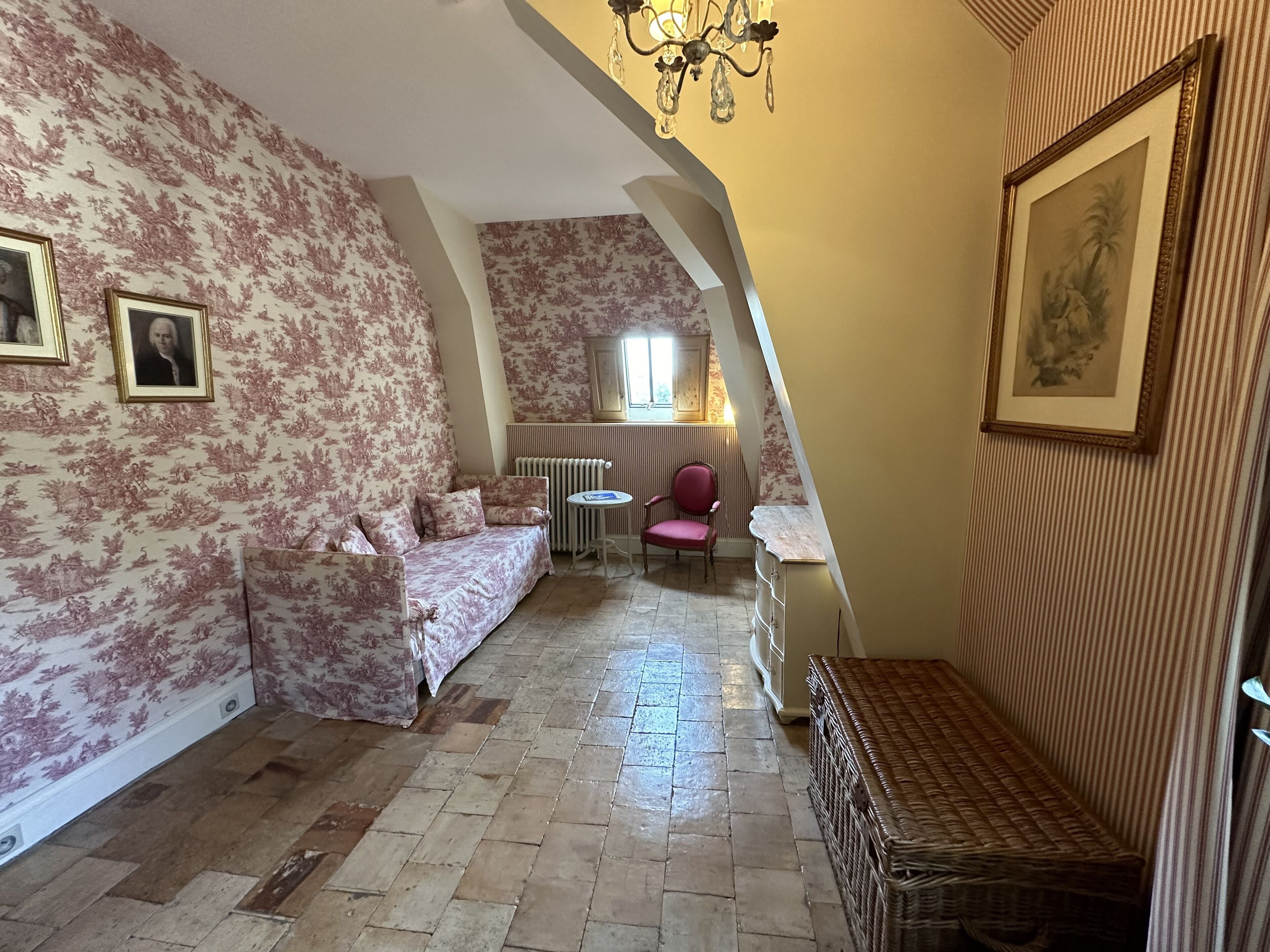 A cozy room with a floral-patterned sofa, a small round table, a wicker bench, and a framed picture on the wall.