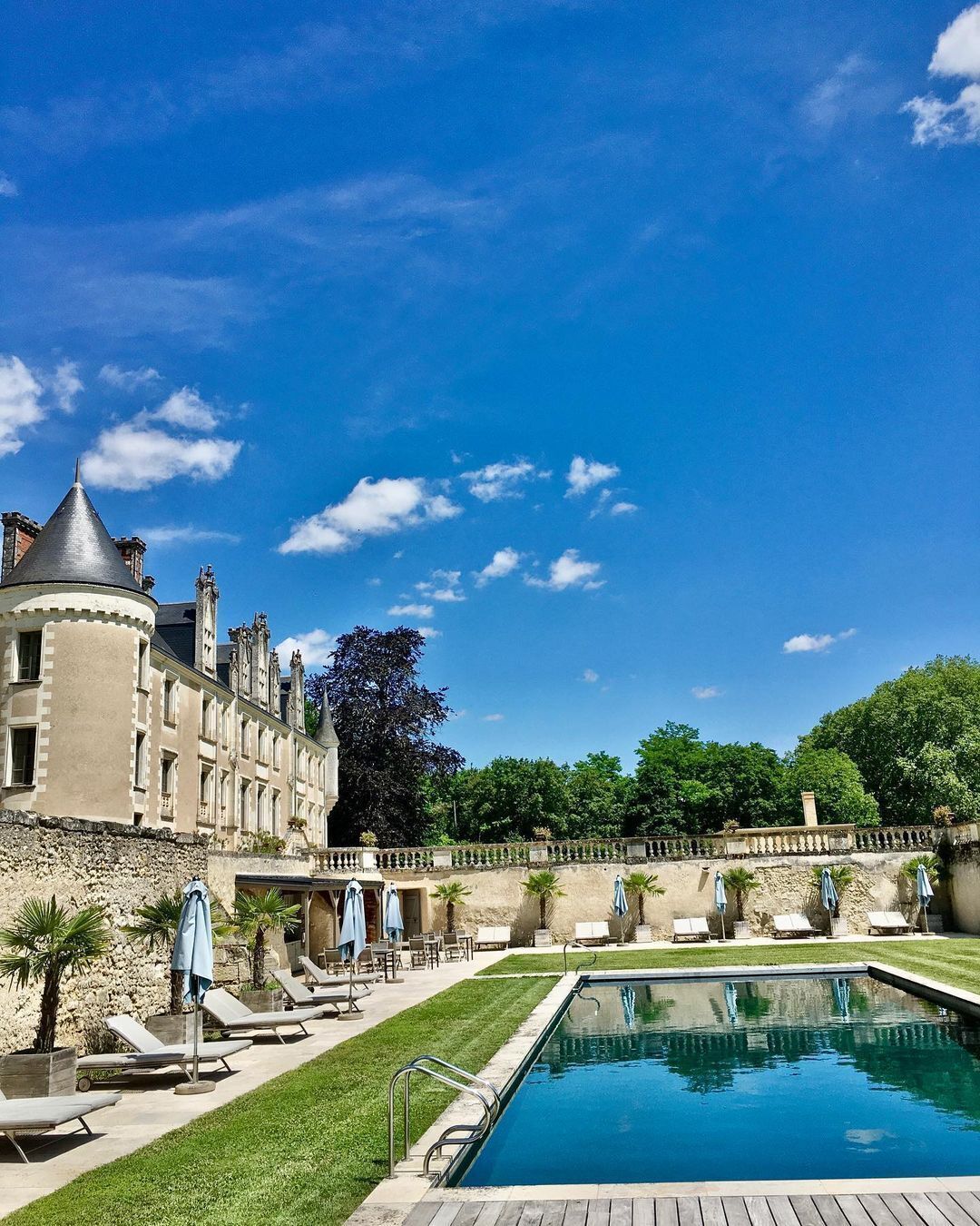 A pool area with lounge chairs and umbrellas, a large building with a turret, and a clear blue sky.