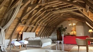 An attic bedroom with a large bathtub, a bed, and a red sofa. - Château des Arpentis (Saint-Regle)