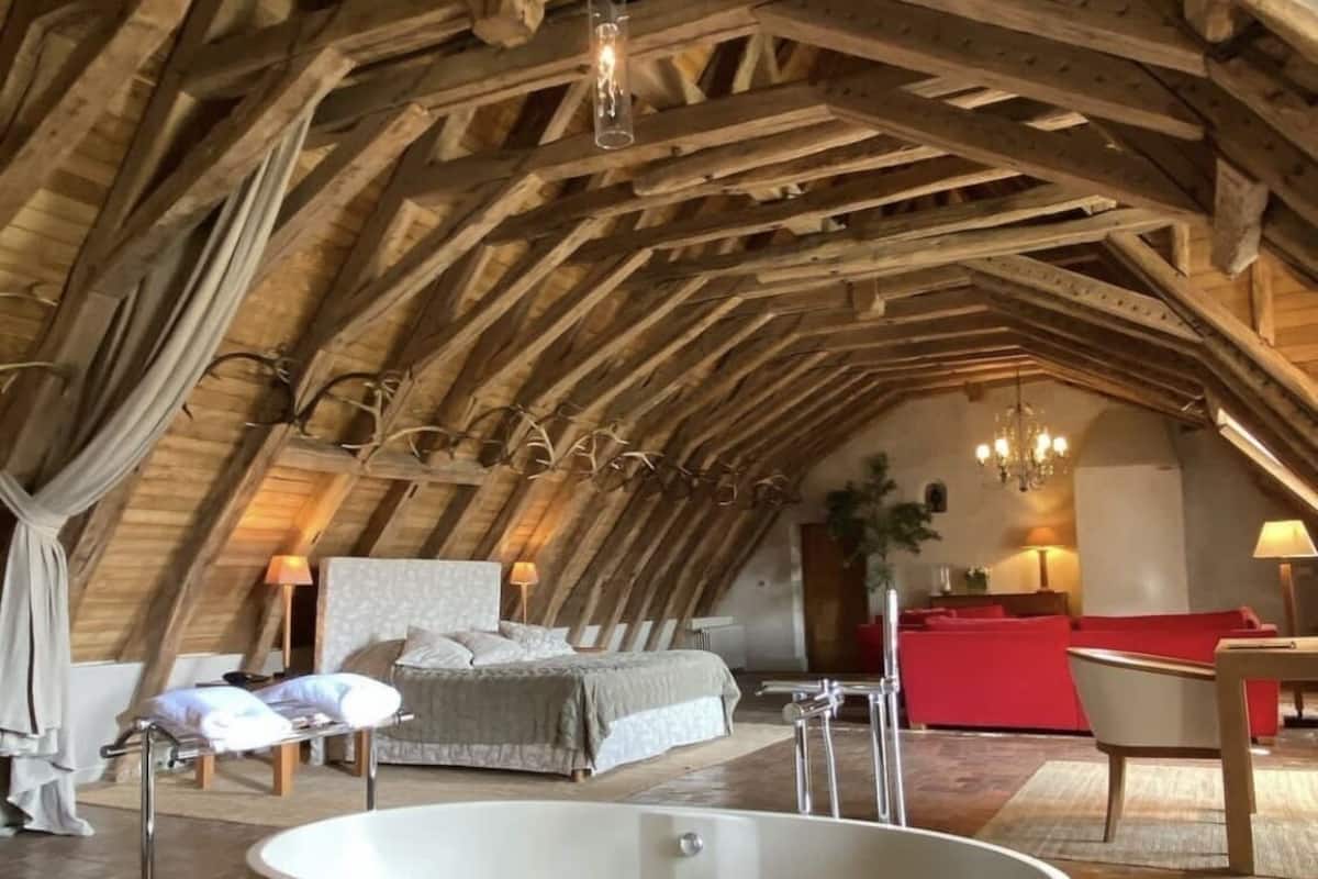 An attic bedroom with a large bathtub, a bed, and a red sofa.