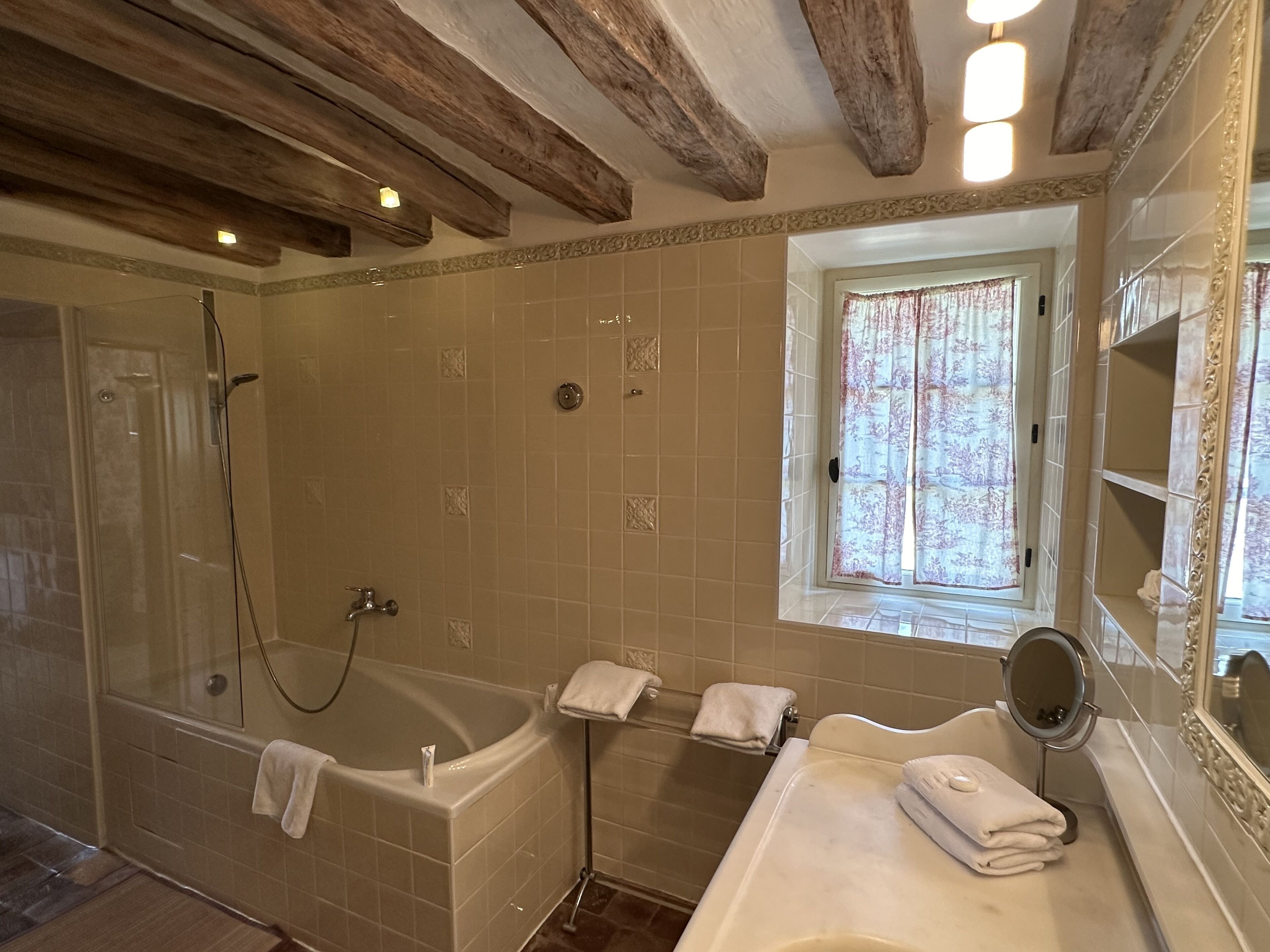 A bathroom with a bathtub, a shower, a vanity with a mirror, and a window with curtains.