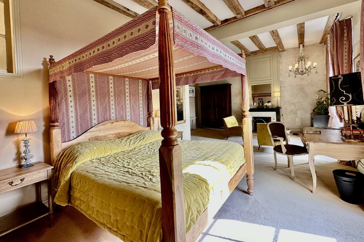 A four-poster canopy bed with a green bedspread, wooden furniture, and a chandelier.