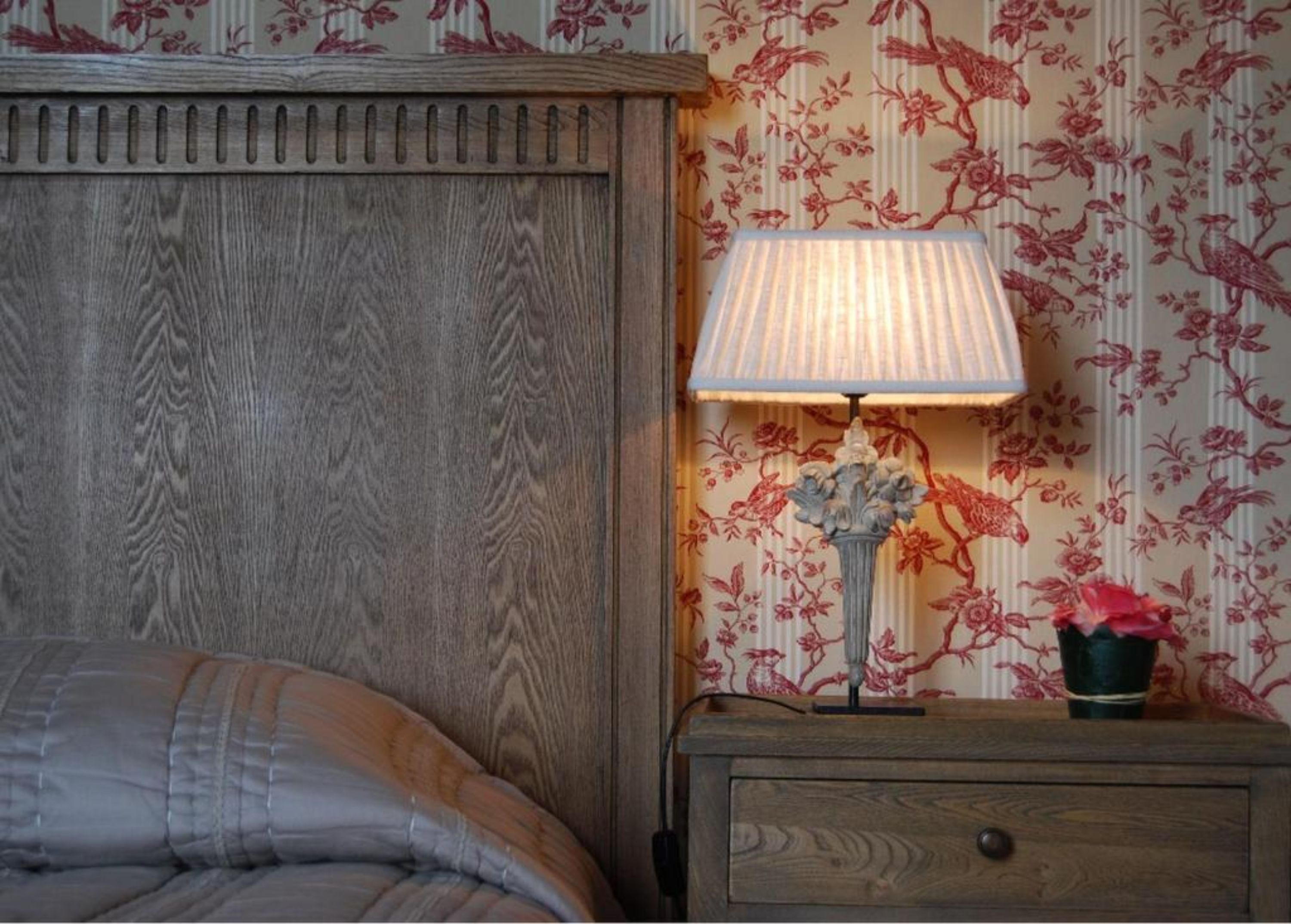 Un dormitorio con cabecera de madera, una mesita de noche con lámpara y papel tapiz floral.