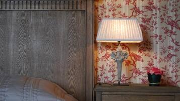 A bedroom with a wooden headboard, a nightstand with a lamp, and floral wallpaper.