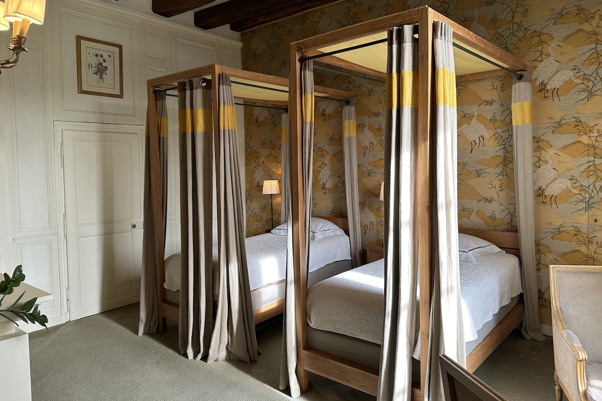 A four-poster bed with a canopy, a bedside table with a lamp, and a wall with a floral wallpaper pattern.