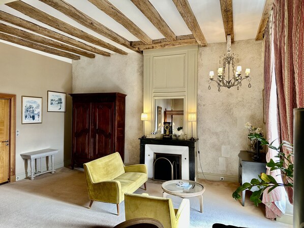 A room with a fireplace, a yellow armchair, a round table, and a wooden cabinet. - Château des Arpentis (Saint-Regle)