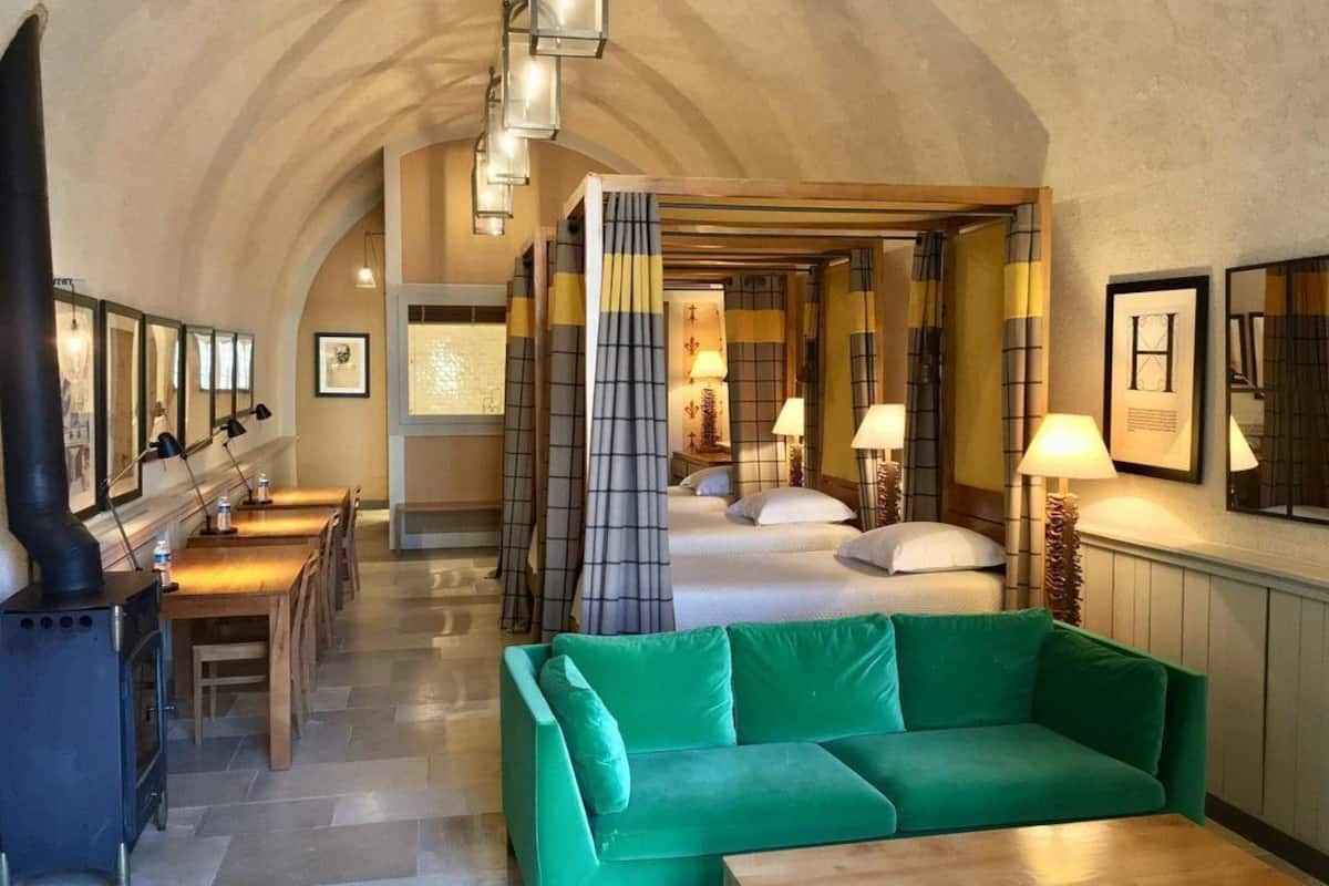 A hotel room with a green sofa, a wooden table, a bed with white linens, and a fireplace.